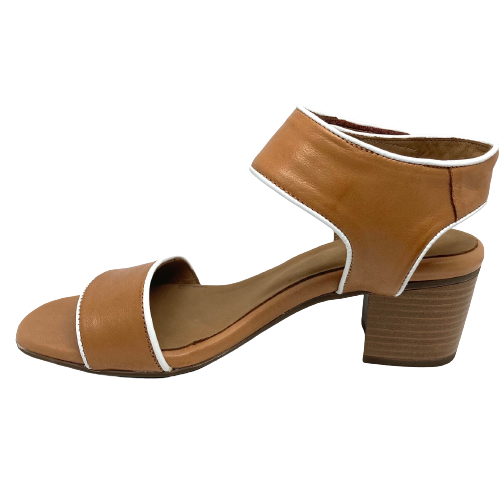 A mid heeled block sandal in tan and piped in white leather. The wide Y back straps around the base of the ankle and is fastened with velcro for convenience.