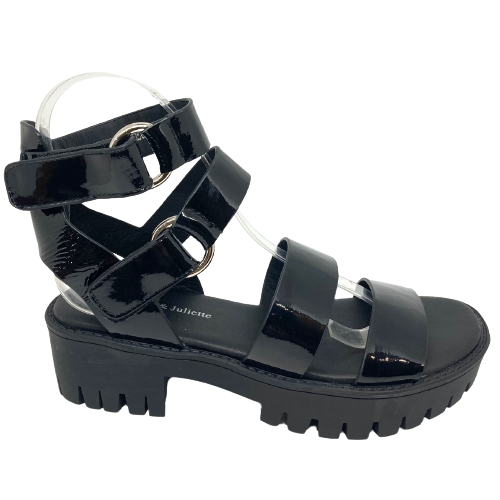 A gladiator inspired sandal in black patent has a chunky black sole, soft footbed and is fastened at the ankle with velcroe and two silver rings. Made by Django & Juliette.