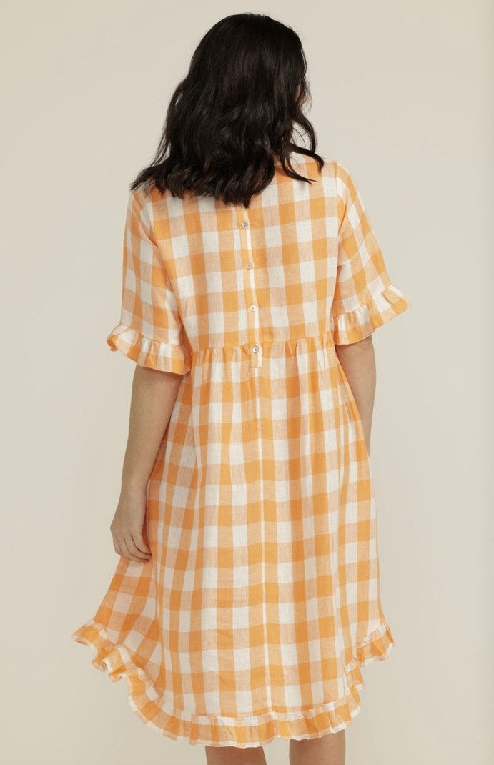 This 100% linen apricot gingham dress is light and cool for our summer months. It has a round neck, a yoke from which a flared bottom falls, buttons at the back and a swooped hemline. The short sleeve and the hemline are finished with a 6cm ruffle. And there are also pockets!