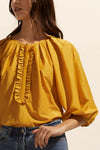 Soft gathering off the neckline creates a curved and feminine aesthetic in this piece. Neat ruffles frame the ¾ placket providing poise and polish.    Colour: Ochre