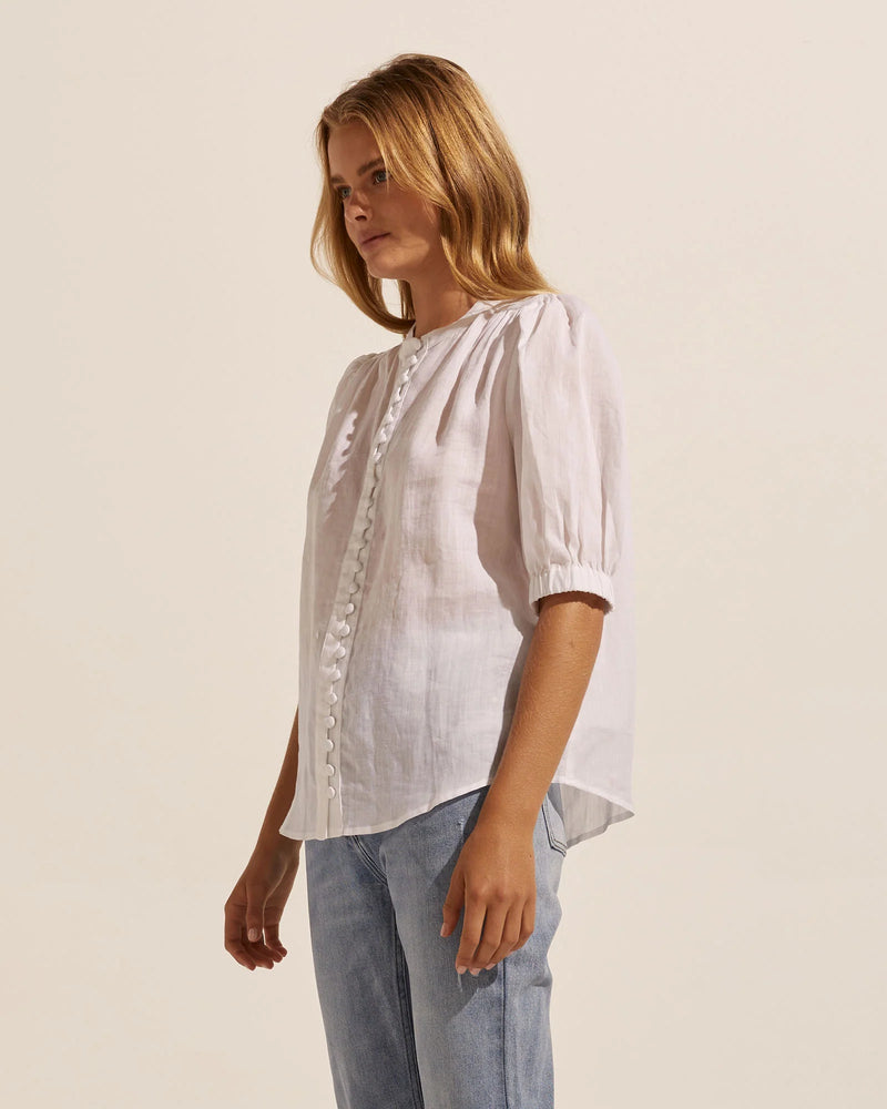 This simple yet elegant piece is a study in relaxed yet feminine dressing. The button-through style has slight gathering off the front shoulders and rear yoke creating an effortless aesthetic.   A subtle blouson sleeve, cuffed just above the elbows is finished with a neat elastic band. The body shape offers a neat fit making this piece the perfect spring companion.