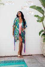 Made by Possi of softly flowing 100% viscose this beautiful kimono will have you feeling cool, comfortable and elegant on your next vacation. This tropical print fabric is available in orange or emerald with a contrasting striped tie belt.  Sizes  -  S/M  L/XL